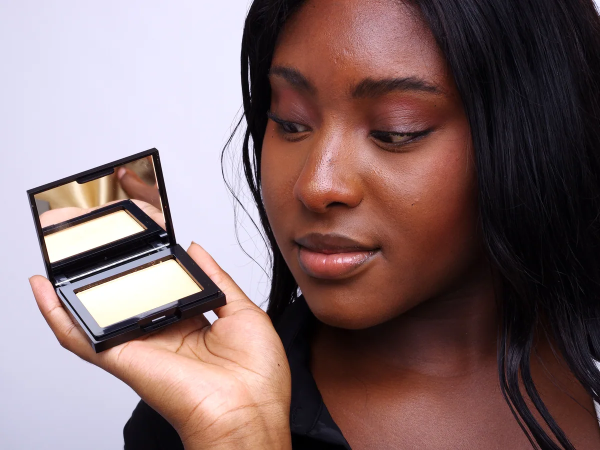 Highlighter doré NEW BLACK, boîtier ouvert près d’une peau noire