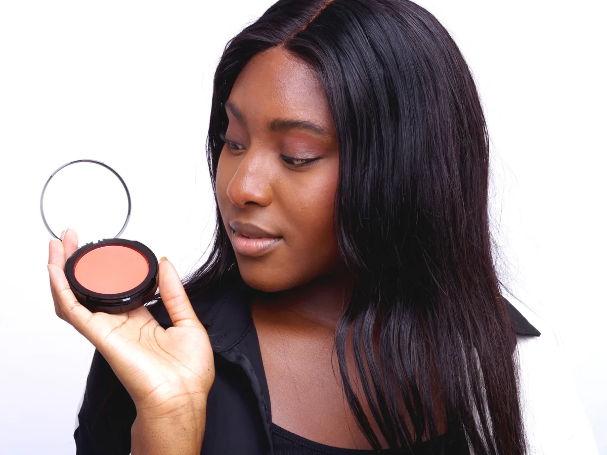 Femme noire tenant un boîtier de poudre compacte ouvert